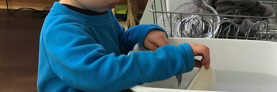 Toddler child putting dirty dishes in a dish pan