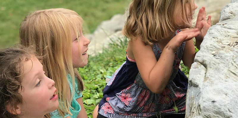 three kindergarten aged children hiding behind and peering over the top of a large rock