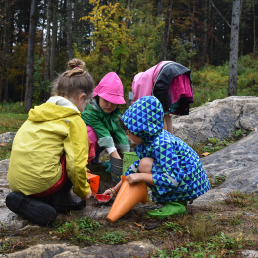 children in rain gear, playing on rock