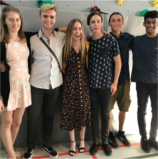 Six graduates in front of rock climbing wall