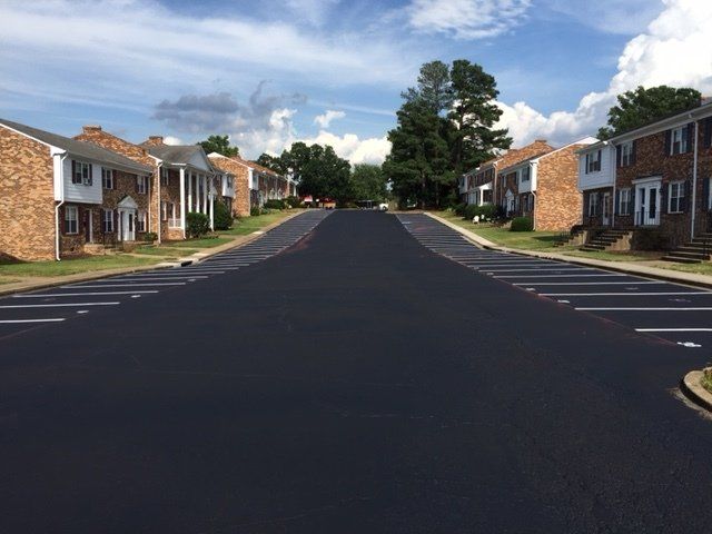 A freshly paved asphalt parking lot lined with white parking spaces between two rows of brick apartment buildings.