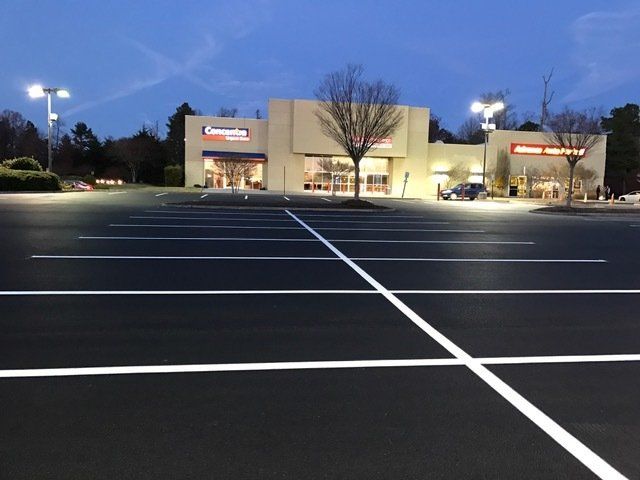 Empty parking lot in front of two commercial storefronts during twilight.