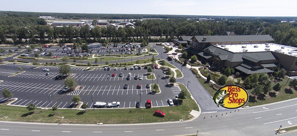 Aerial view of a Bass Pro Shops retail store, its parking lot, and surrounding roads on a sunny day.