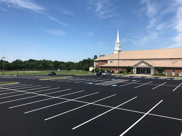 A freshly paved parking lot with white painted lines in front of a church building under a clear blue sky.