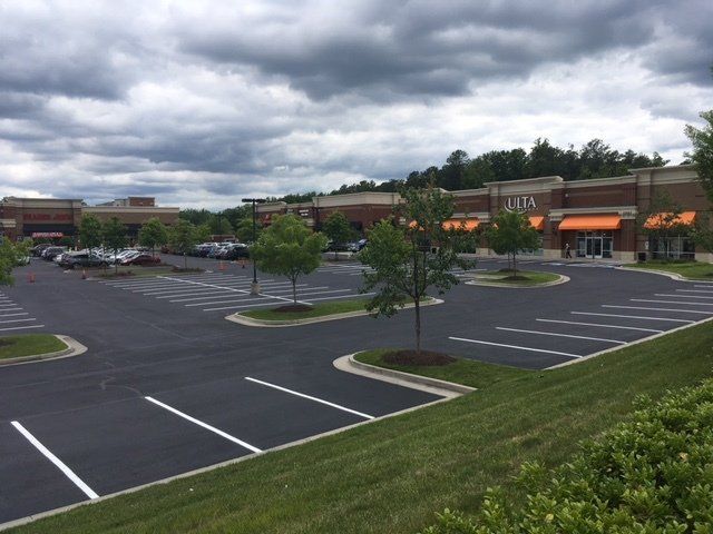 A modern commercial strip mall featuring storefronts with orange awnings, a paved parking lot, and green landscaping.