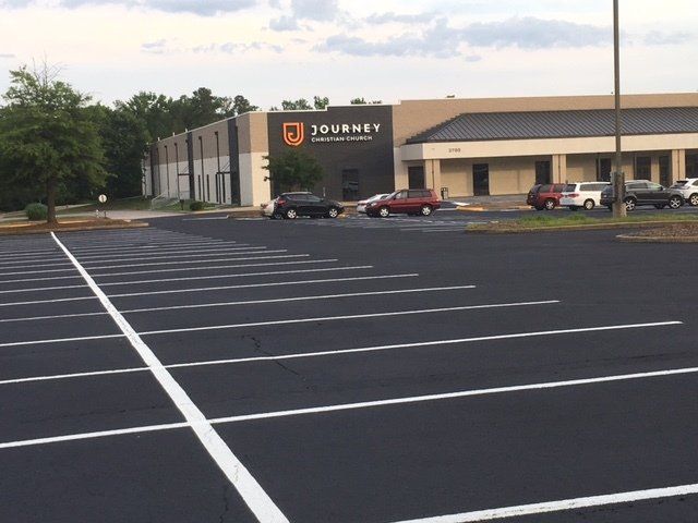 A paved parking lot with white painted lines in front of a tan commercial building labeled Journey Christian Church.