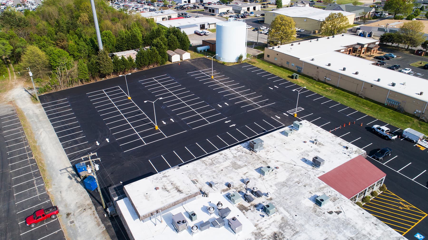 Aerial view of a freshly paved parking lot with marked white lines next to a commercial building and a water tower.