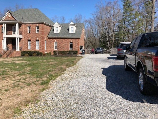 A large brick house with a gravel driveway in front of it.