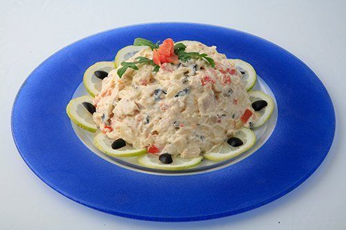 Insalata di pasta cremosa su un piatto blu, guarnita con pomodoro ed erbe aromatiche.