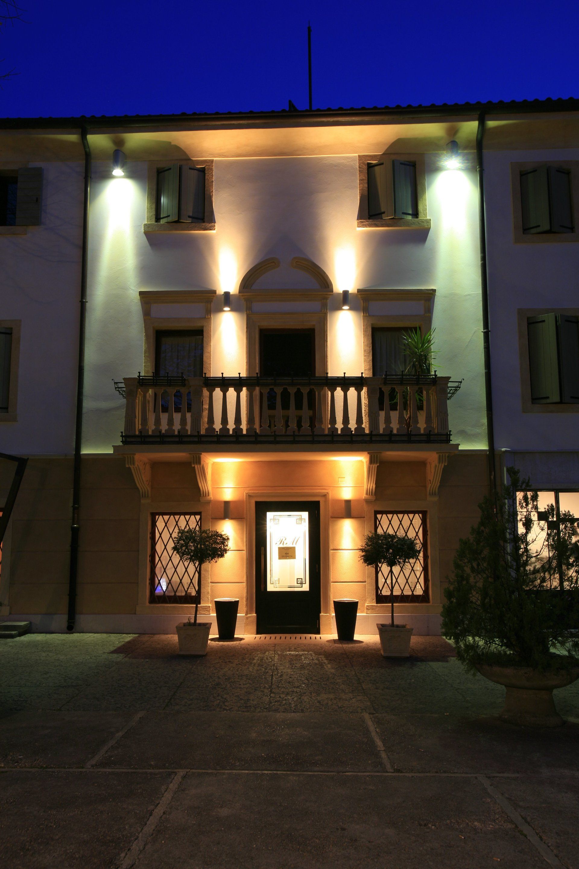 Ingresso dell'edificio illuminato di notte con luci calde e porta centrale sotto i balconi