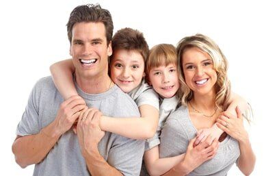 Family Smiling - Sacrey & Sacrey Dentistry in Geneva, IL Family of four smiling, hugging in front of a white background.
