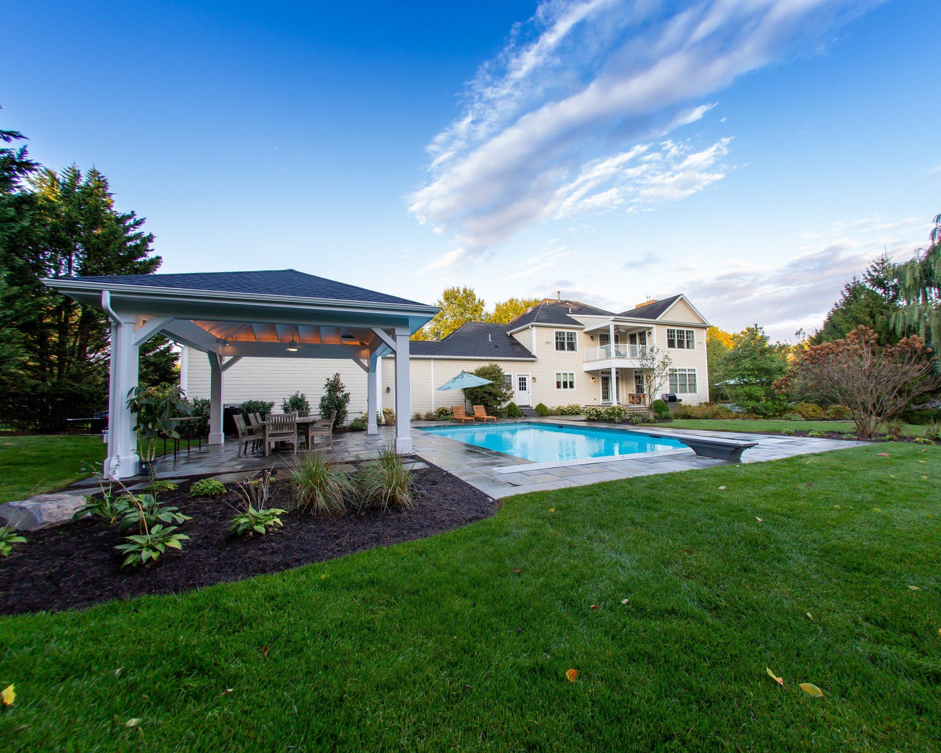 Backyard with pool, gazebo, and two-story house, under a blue sky with clouds.