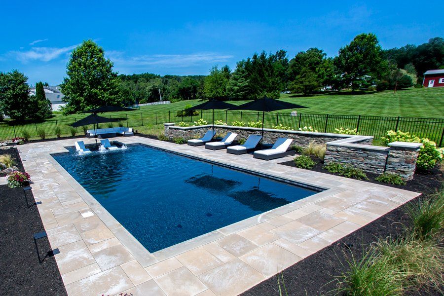 Rectangular pool with lounge chairs, umbrellas, and landscaping on a sunny day.