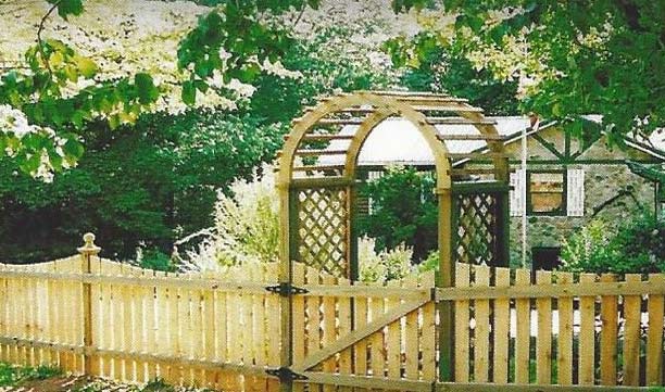 Wooden arbor gate and picket fence in a lush garden with a small shed behind it