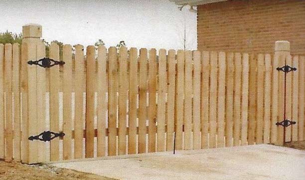 Wooden picket fence gate with black hinges in a paved outdoor area