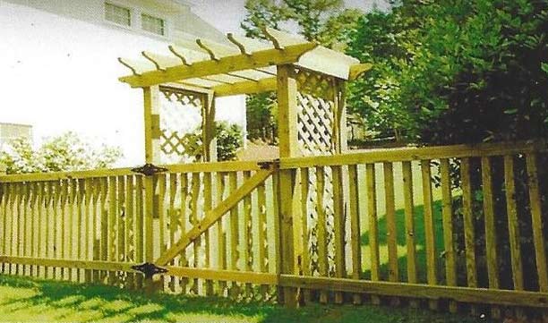 Wooden backyard gate and trellis fence with a small arbor in a sunny garden