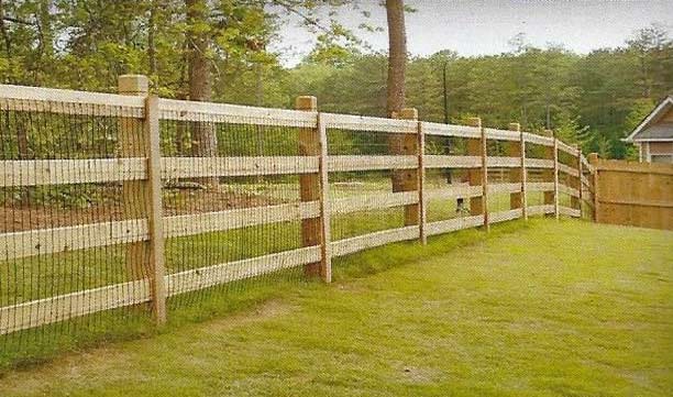 Wooden split-rail fence beside a green lawn with trees in the background.