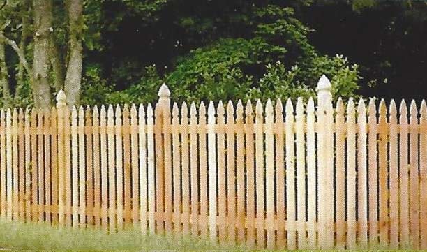 Wooden picket fence in front of leafy trees and grass