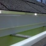 Dripedgeextension3 A close-up view of a white metal rain gutter installed along the edge of a gray shingled roof.