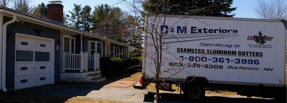 A D&M Exteriors trailer parked in front of a house with a white garage door, advertising seamless aluminum gutters.