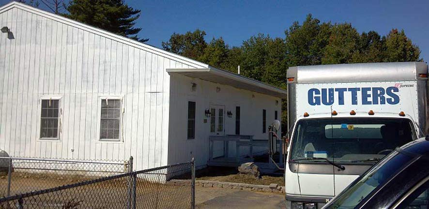 A white, single-story building sits next to a truck with 