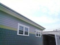 The side of a house featuring blue shingle siding on the bottom, light grey lap siding on top, and two white windows.