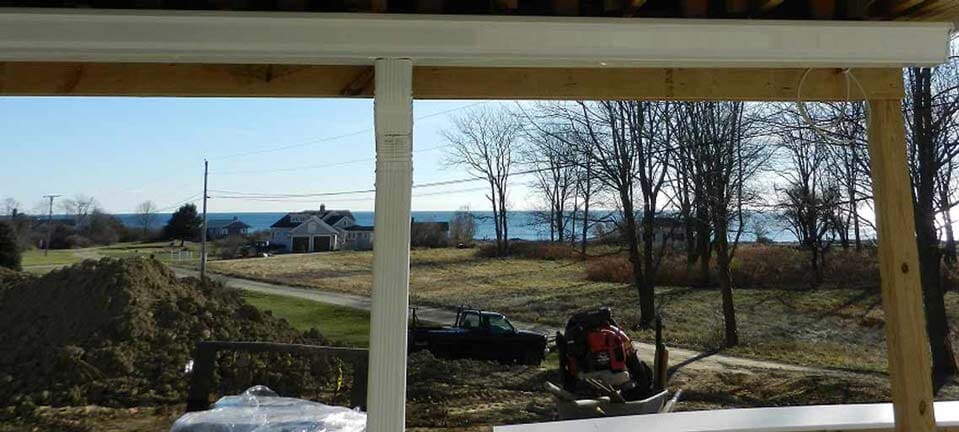 A view of a coastal house and trees from under a wooden porch frame on a sunny day.