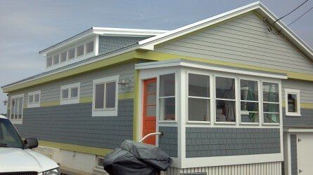 A gray house with two-tone siding, a lime-green accent trim, an orange door, and a white-framed enclosed porch.