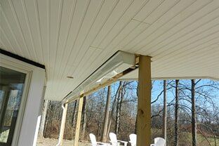 Metal roof gutter in red color - Seamless Gutter in Rochester, NH A long infrared heater mounted to the white beadboard ceiling of an outdoor covered patio with trees in the background.