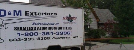 A D & M Exteriors truck parked in front of a house, featuring their company name, contact numbers, and service details.