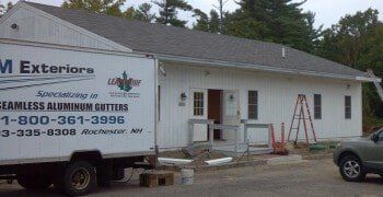 A white exterior services truck parked in front of a white building with a ladder leaning against the wall.