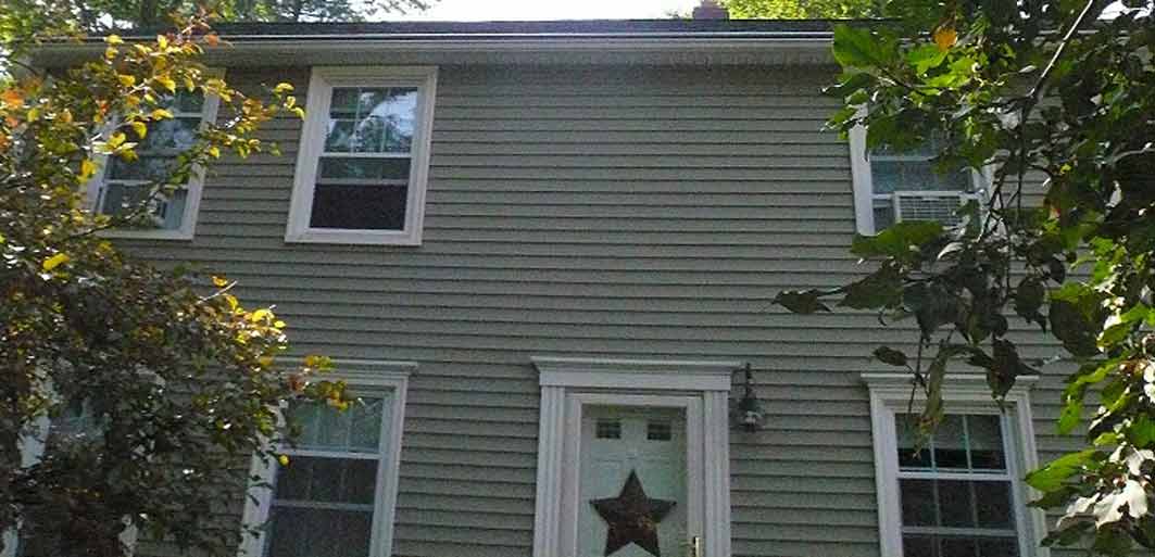 A two-story house with grey, horizontal siding, white trim around windows, and a front door adorned with a metal star.