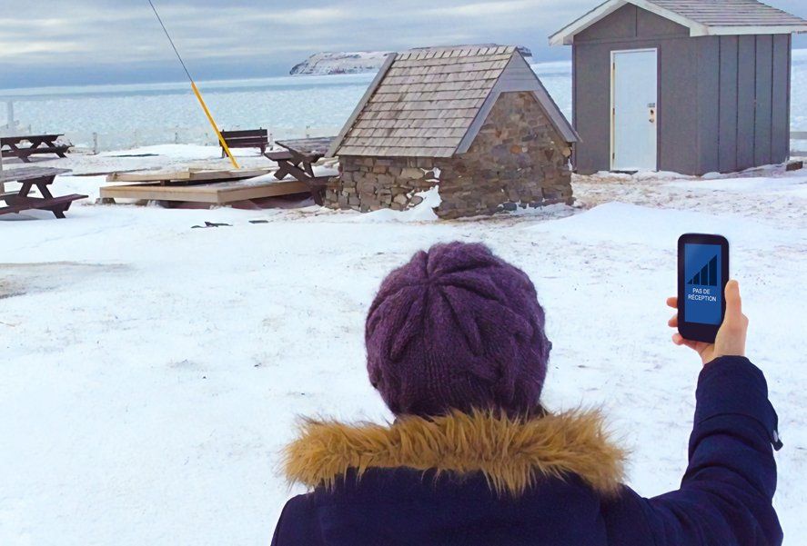 Image d'une femme regardant son téléphone cellulaire affichant des barres de réception. Devant elle, un paysage hivernal.