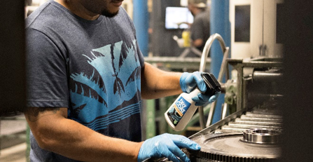 A man is cleaning a gear with a spray bottle in a factory.