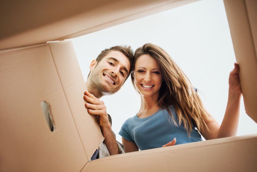 A man and a woman are looking out of a cardboard box.