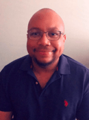 A bald man wearing glasses and a blue polo shirt is smiling for the camera.