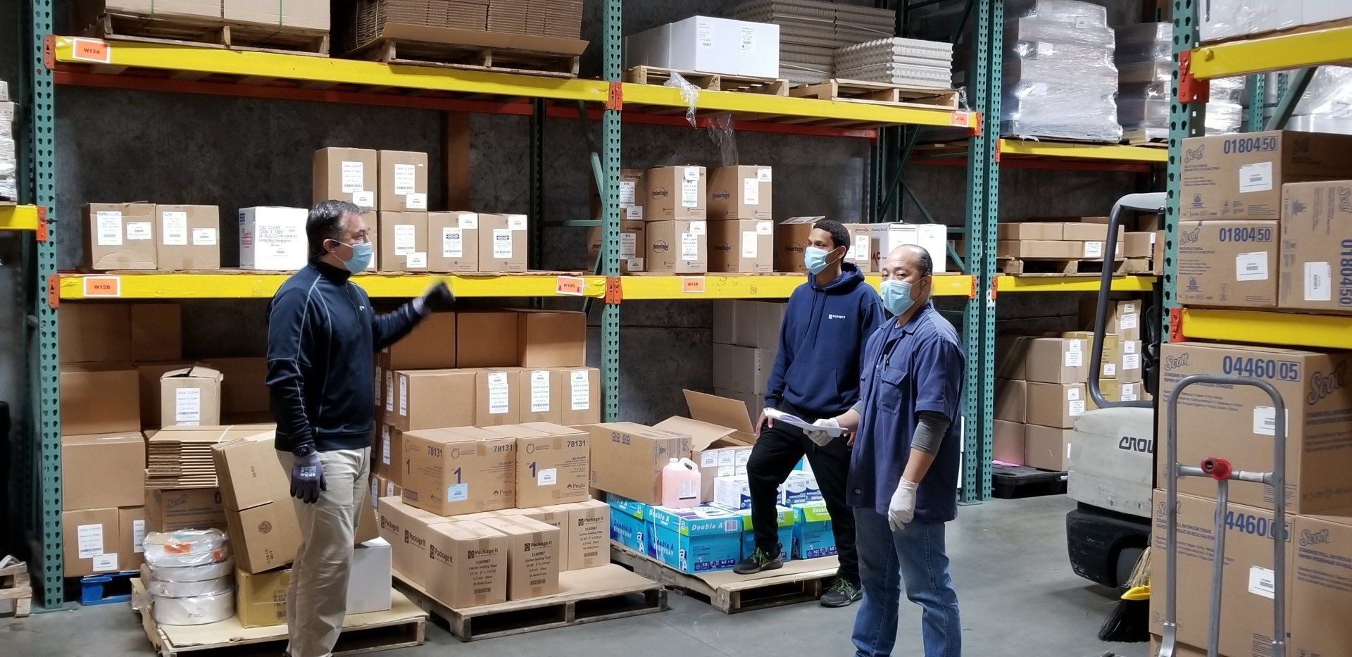 A group of people wearing masks are standing in a warehouse.