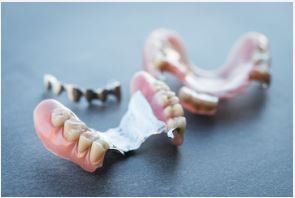 Three dental prosthetics, including a partial denture with a metal framework, resting on a dark surface.