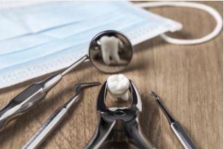 Dental tools and a tooth on a wooden surface, with a dentist’s mirror reflecting a tooth and a surgical mask in the back.