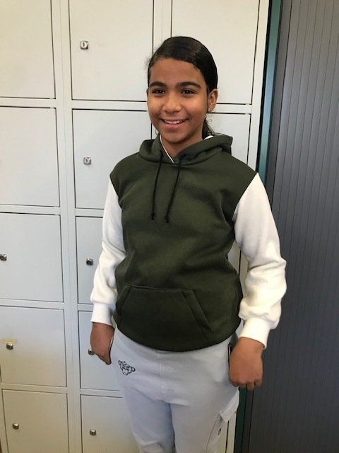 Een meisje in een groen-witte hoodie lacht terwijl ze voor de kluisjes staat.