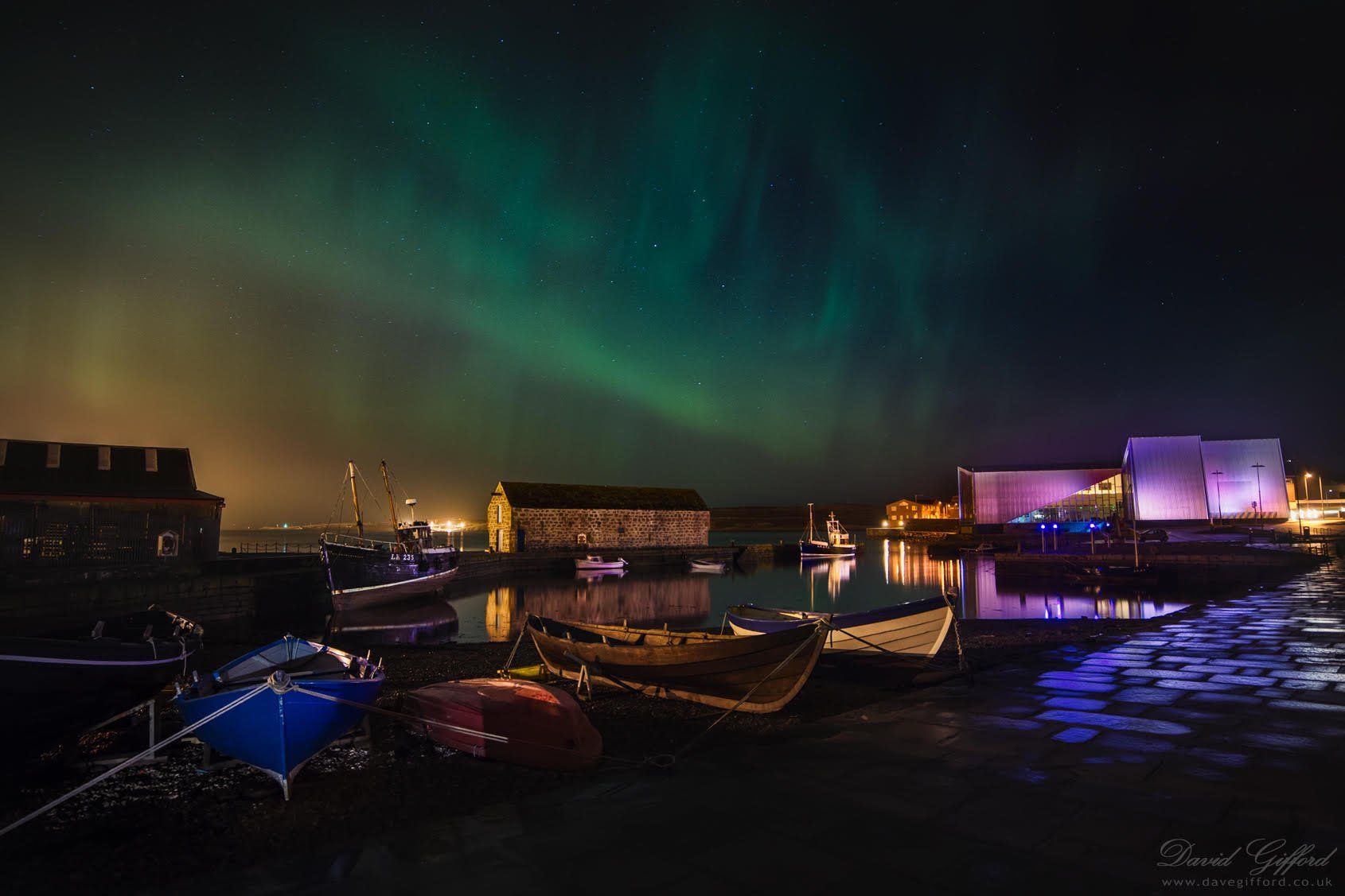 The aurora borealis is shining over a harbor at night.