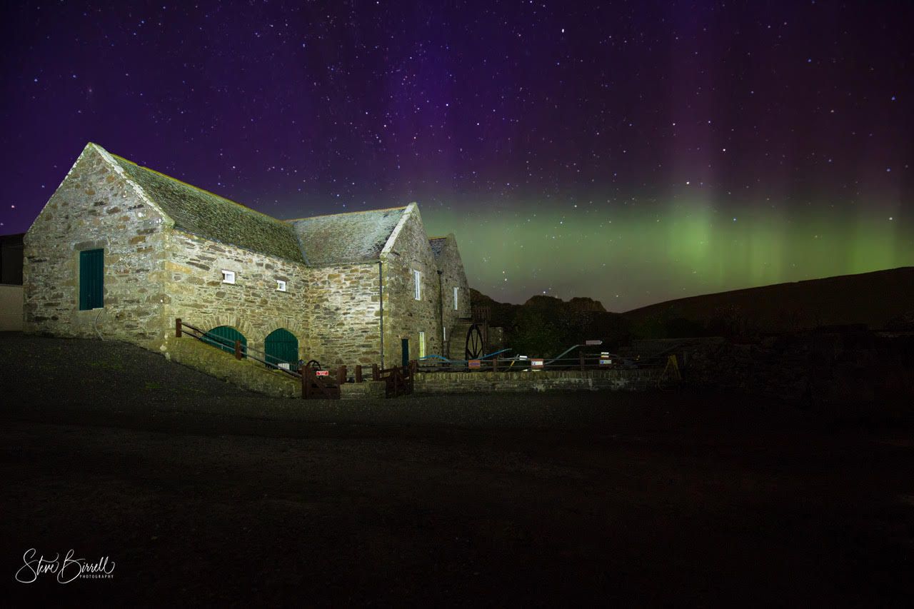 The northern lights are shining over a stone building at night.