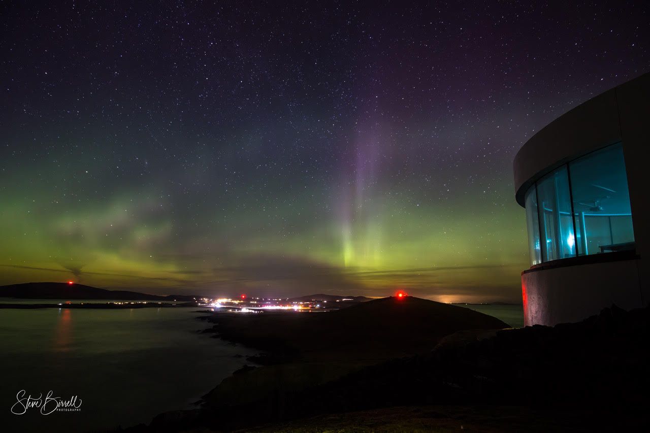 The aurora borealis is visible in the night sky over a body of water.