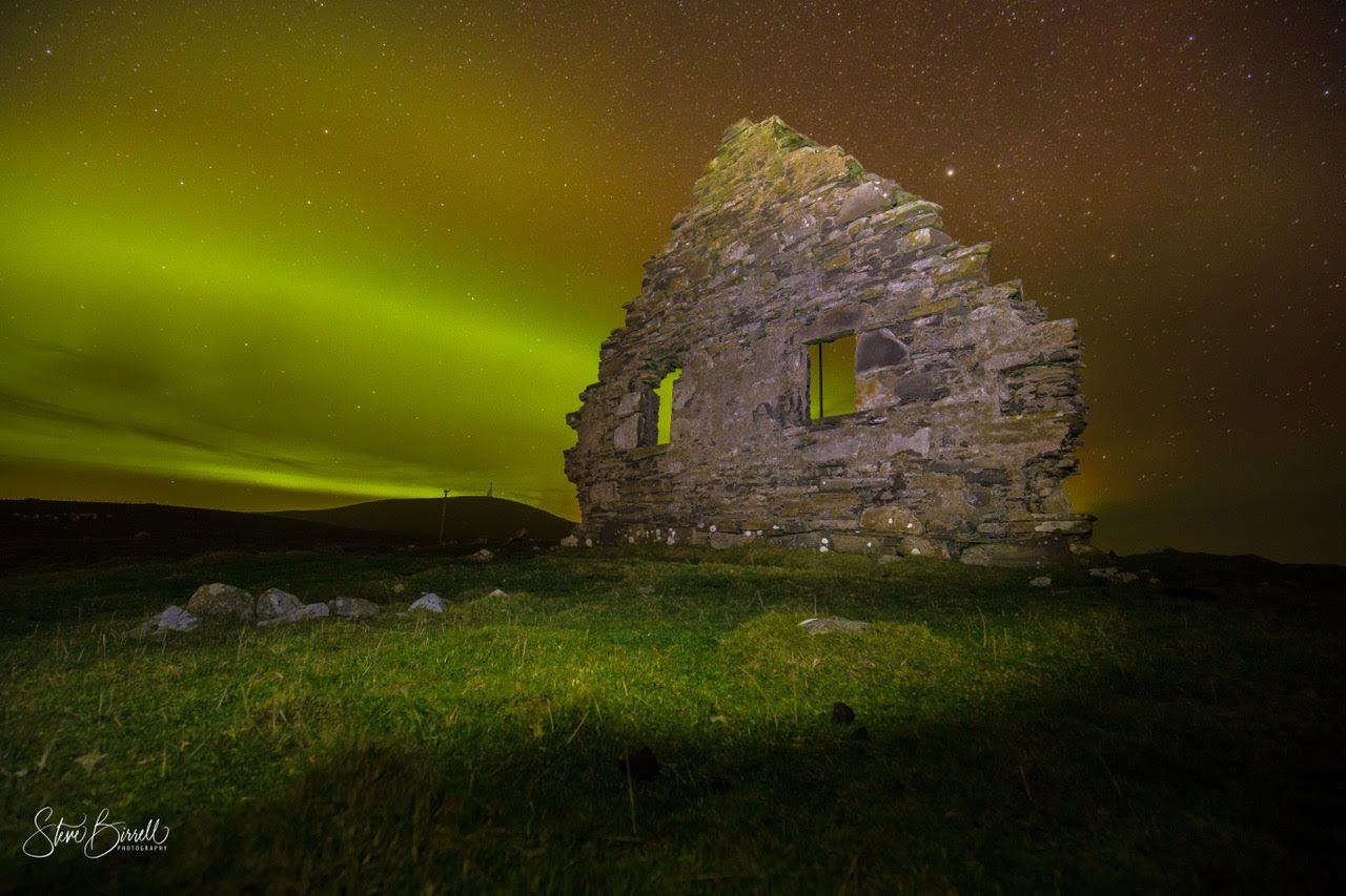 The aurora borealis is shining brightly over an old stone building.