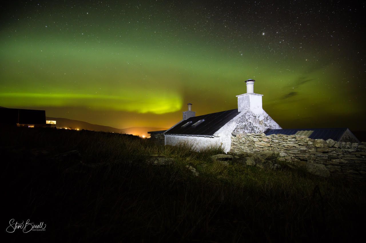 The aurora borealis is shining brightly over a white house.