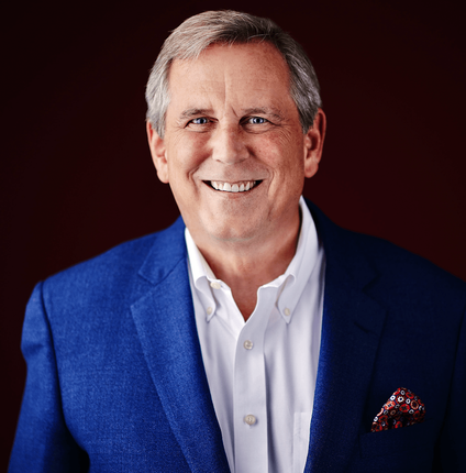 Man in a blue blazer and white shirt smiling at the camera against a maroon background.