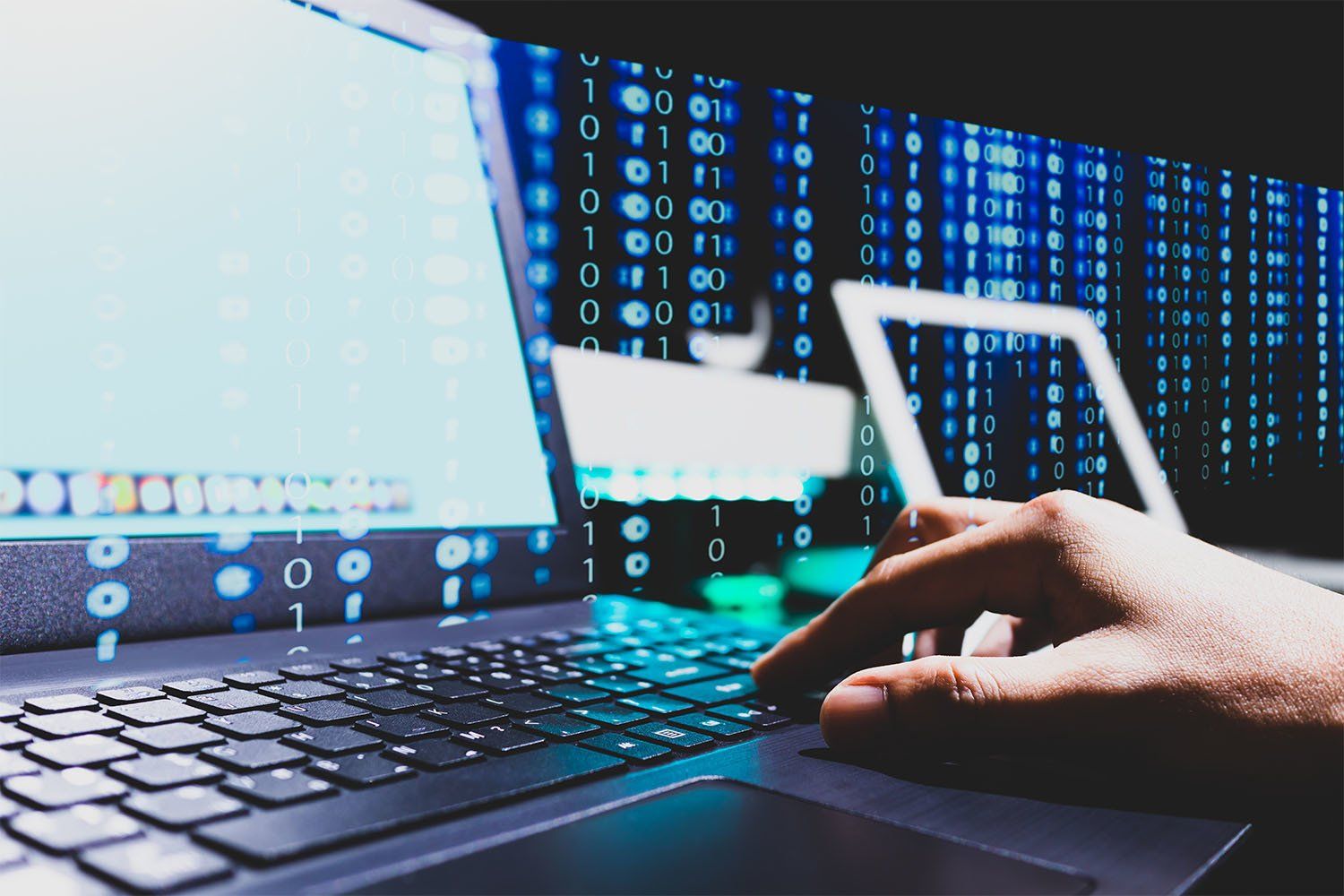 Hand typing on laptop with glowing digital code and devices in the background