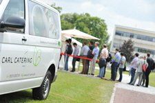 A group of people are standing in front of a carl catering van.
