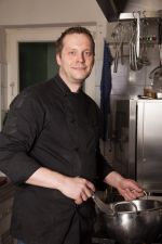 A man in a chef 's jacket is cooking in a kitchen.