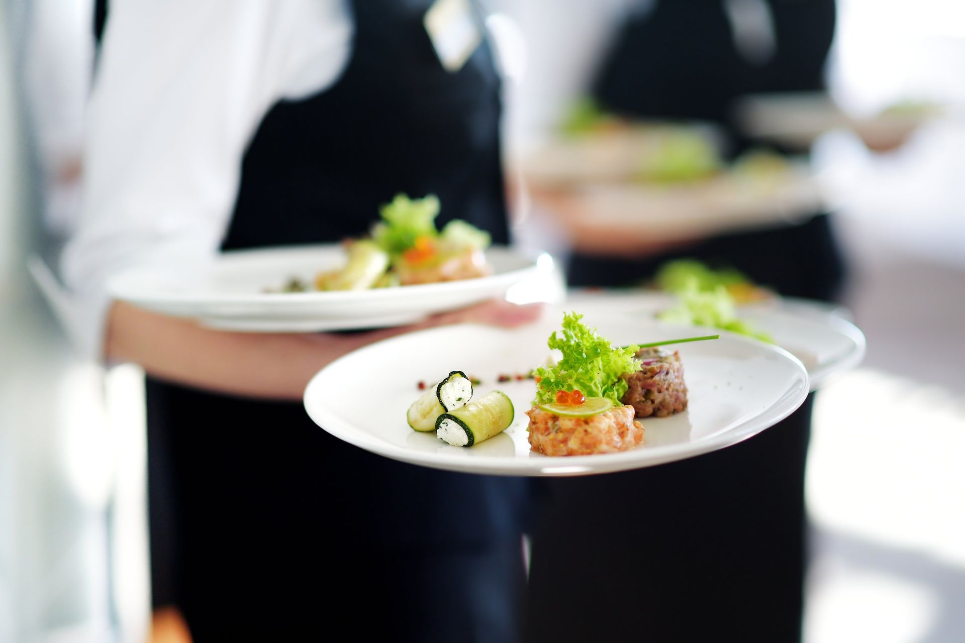 Two waiters are holding plates of food in their hands